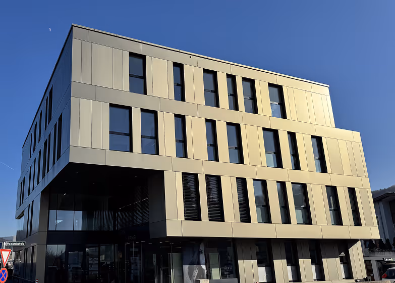 Modernes mehrst&ouml;ckiges Geb&auml;ude mit grauer Fassade und gro&szlig;en Fenstern unter klarem blauem Himmel.