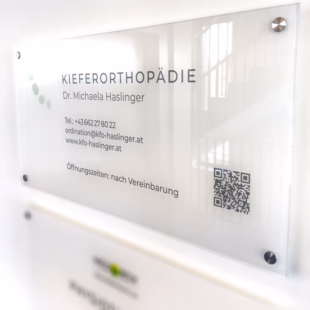 Schild an einer Wand mit der Aufschrift Kieferorthop&auml;die Dr. Michaela Haslinger, Telefonnummer, Email, Webseite und QR-Code.
