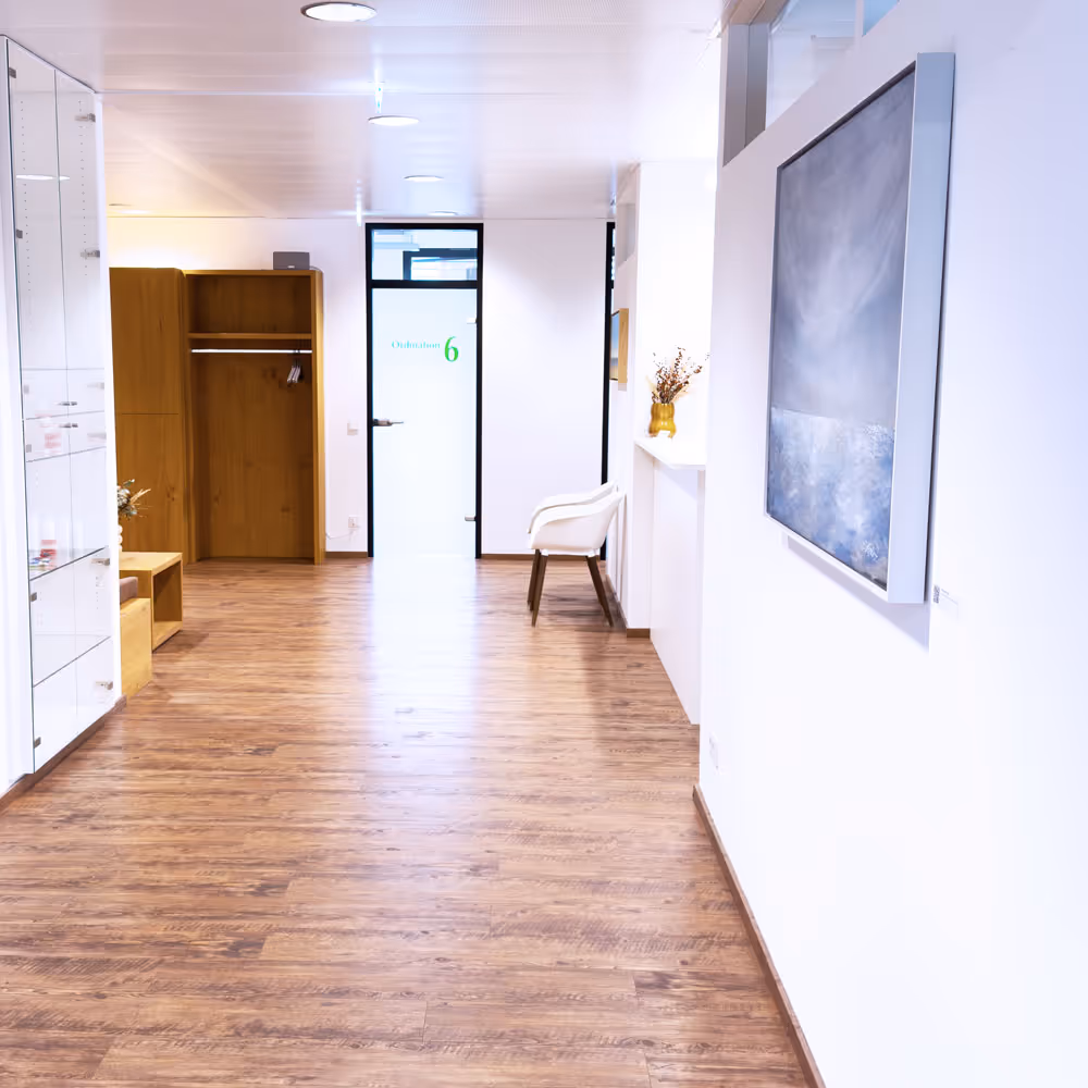 Hell beleuchteter Flur mit Holzfu&szlig;boden, wei&szlig;em Stuhl, offenem Holzschrank und einem Bild an der Wand.