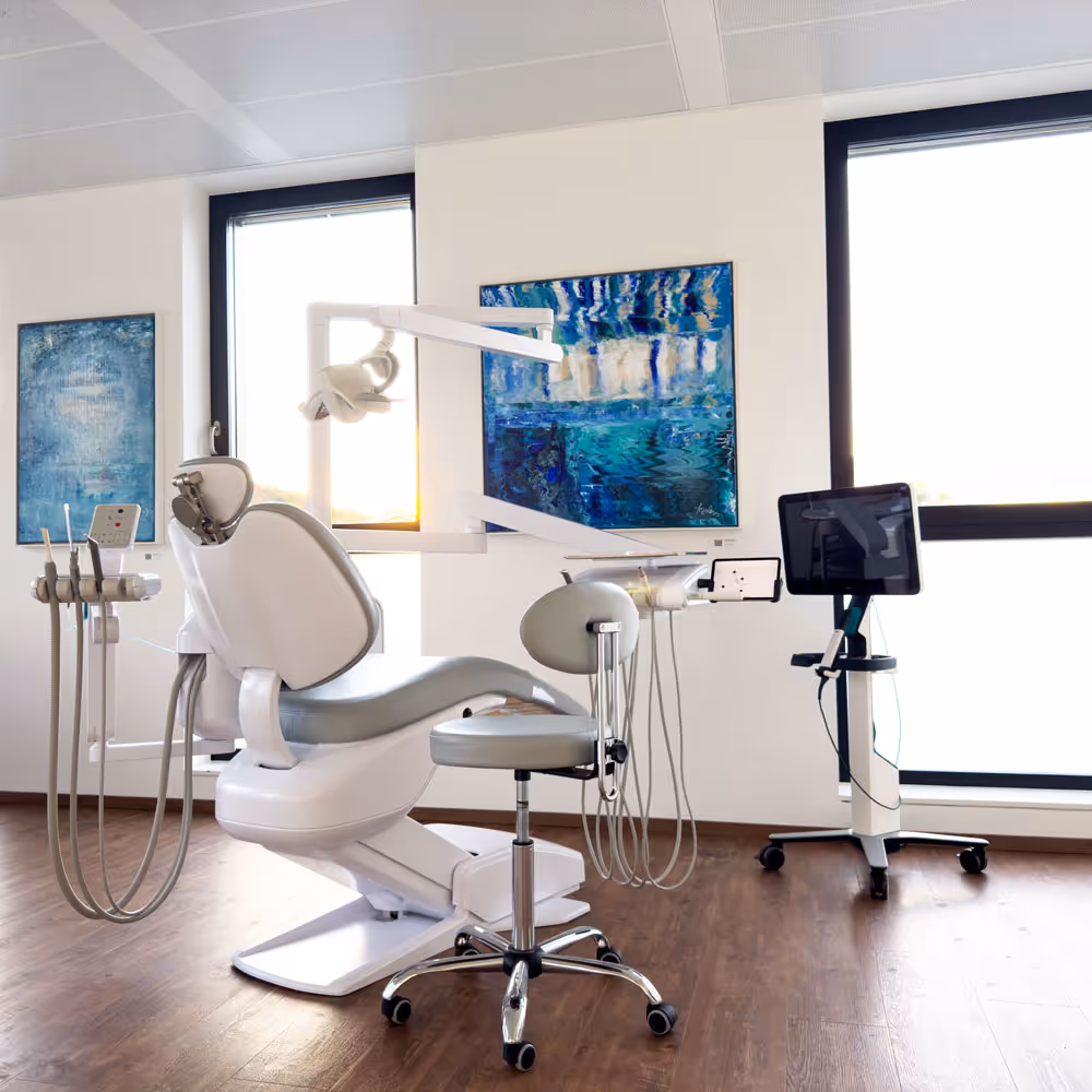 Heller Behandlungsraum mit einem weißen Zahnarztstuhl, Instrumenten und modernem 3D-Scanner vor großen Fenstern.