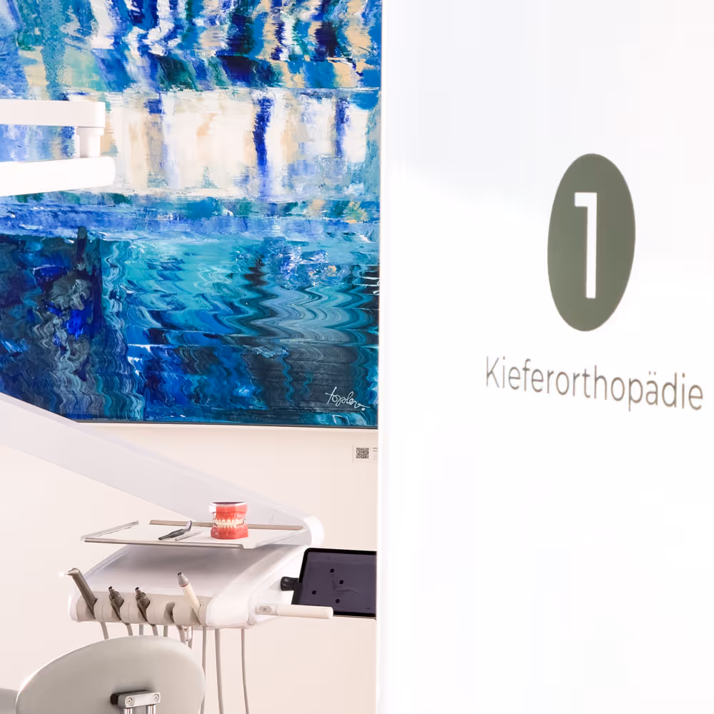 Zahnmedizinischer Behandlungsstuhl und Ger&auml;t vor abstraktem blauen Kunstwerk in Praxis mit T&uuml;rschild Nummer 1 und Aufschrift Kieferorthop&auml;die.
